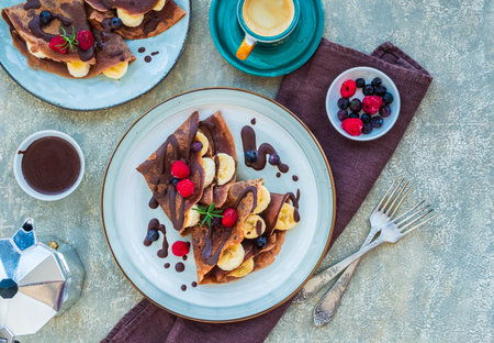 Thin chocolate pancakes stuffed with bananas, raspberries and blueberries, poured with chocolate sauce, on a gray ceramic plate on a light concrete background. Pancake recipes. Pancake dayの写真素材