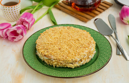 Whole traditional chopped dough Napoleon cake with custard on a green plate on a light concrete...