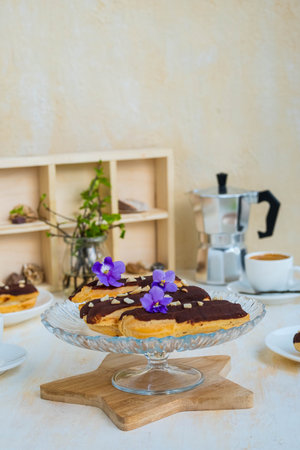 Dessert, choux pastry sweets with vanilla custard, covered with chocolate glaze, on a glass stand on...