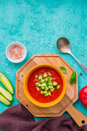 Tomato gazpacho, traditional Spanish cold soup or appetizer in a yellow clay bowl on a wooden board against a turquoise concrete background. Cold soup recipes. Spanish foodの写真素材