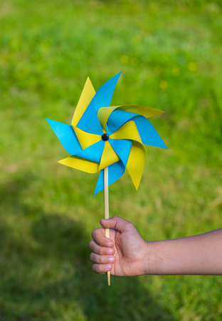 A boy plays with a yellow and blue paper 8-petal weather vane in the garden. Children's creativity, crafts. DIY conceptの写真素材