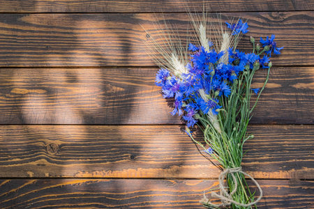 A bouquet of cornflowers and ears of wheat or rye on a brown wooden background. Blooming, flower bouquets. Top view, copy spaceの写真素材