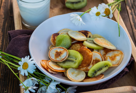 Mini pancakes with sliced kiwi in a ceramic bowl on a wooden tray on a wooden concrete background. Pancake recipes. American cuisine.の写真素材