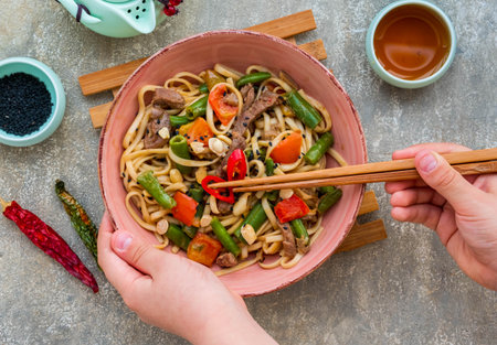 Wok noodles with beef, green beans and bell peppers in a pink bowl on a gray concrete background. Chinese cuisineの写真素材