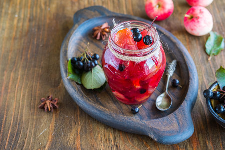 Apple jam with apple pieces and chokeberry in a jar on a brown wooden background. Jam recipes. Canning, harvest of apples.の写真素材