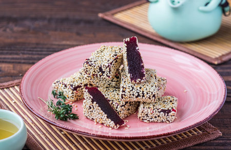Sweetness, square marmalade beetroot candy in sesame sprinkling on a pink plate on a brown wooden...