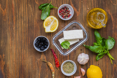 Prepared ingredients for cooking marinated feta with spices and olives in oil on a brown wooden background. Cheese appetizer recipes. Greek cuisineの写真素材