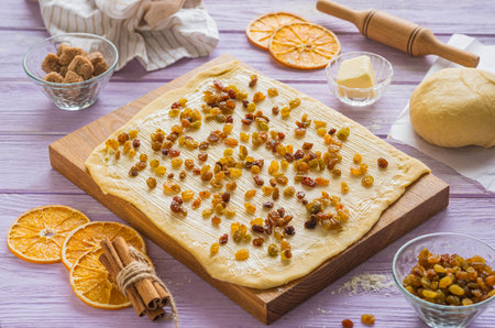 Step-by-step cooking of kraffin ( cruffin), yeast Easter cake with raisins. Step three, sprinkle raisins on the rolled out dough on a wooden board.の写真素材