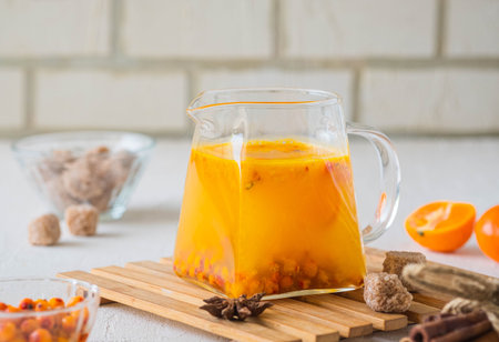 Hot drink, sea buckthorn tea with tangerine slices in a transparent glass teapot on a light concrete...