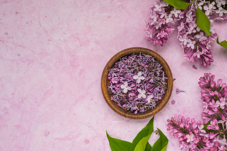 Ingredient, plucked lilac flowers in a wooden bowl and spoon prepared on a pink concrete background. Use of edible wild plants and flowers in cooking or aromatherapy. top view, copyspaceの写真素材
