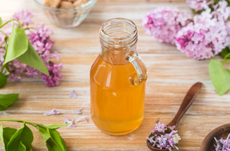 Lilac flavored sugar syrup for lemonades, ice cream or biscuits in a glass bottle on a light wooden background. Natural flower ingredients for cooking.の写真素材