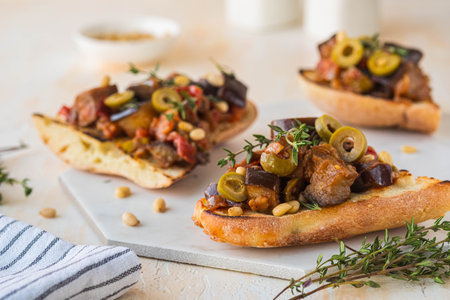 Sicilian caponata, eggplant, tomato and olive stew on white bread on a marble board against a light concrete background. vegetable appetizer. Italian foodの写真素材