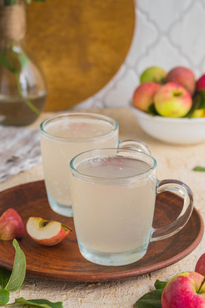 White kvass, a fermented drink made from apples in glass mugs on a light concrete background....
