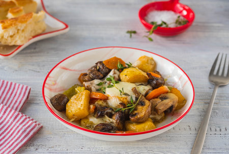 Baked vegetable mix of carrots, turnips and onions with mushrooms and cheese in a white plate on a light wooden background. vegetable recipes. healthy foodの写真素材