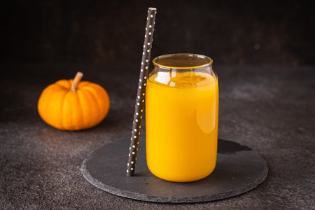 Pumpkin juice with ice in a transparent glass glass on a black slate stand on a black concrete background. vegetable juices. Thanksgiving, Halloween conceptの写真素材