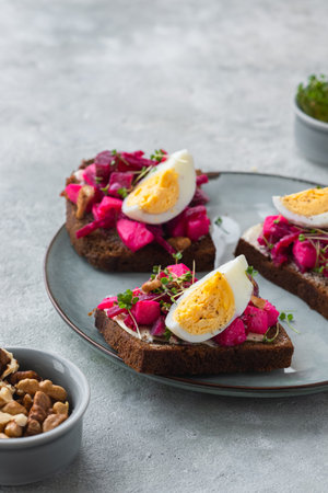 Open sandwiches on rye bread with beetroot salad, boiled egg and microgreens on a ceramic plate on a gray concrete background. swedish food. Sandwich Recipesの写真素材