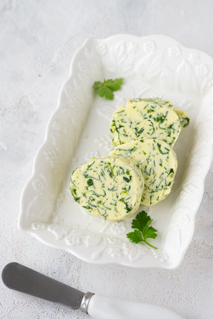 Butter with parsley and salt, cut into circles, on a white rectangular plate on a light concrete background. Types of butter for serving dishes. french cuisineの写真素材
