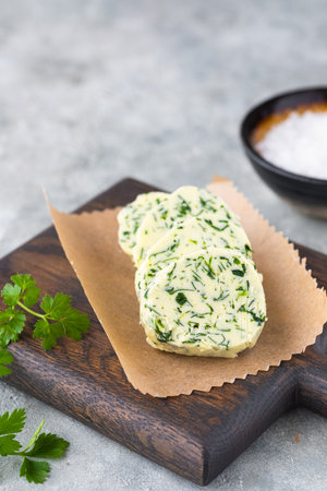 Butter with parsley and salt, cut into circles, on a brown wooden board on a gray concrete background. Types of butter for serving dishes. french cuisineの写真素材