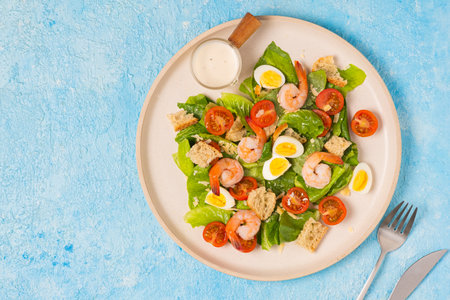 Caesar salad with romaine lettuce, cherry tomatoes, boiled quail eggs and croutons on a light ceramic plate on a blue concrete background. american food. Recipes Seafoodの写真素材