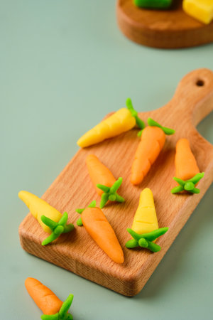 Candies, marzipan carrots handmade from colored marzipan on a wooden mini board on a plain green vinyl background. Sweets, edible decor for cakesの写真素材