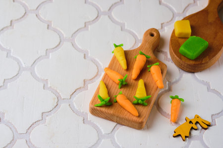 Candies, handmade marzipan carrots from colored marzipan on a wooden mini board on a textured white tile-like background. Sweets, edible decor for cakesの写真素材