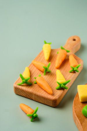 Candies, marzipan carrots handmade from colored marzipan on a wooden mini board on a plain green vinyl background. Sweets, edible decor for cakesの写真素材