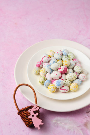 Sugar candy in the form of bird eggs on a white plate on a pink concrete background. Easter concept.