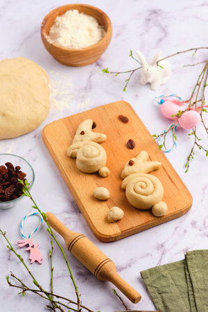 Step by step cooking of Easter Bunny Buns on a light background. Step two, forming a bun in the form of a rabbit on a wooden boardの写真素材