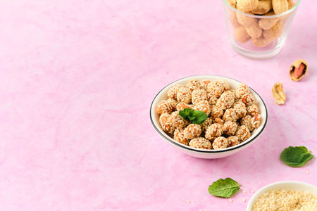 Sweets, peanuts in honey and sesame seeds in a white ceramic bowl on a pink concrete background. Useful sweets; handmade candies. Nut sweetsの写真素材