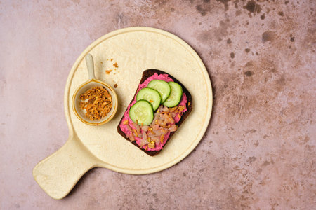 Smorrebrod on rye bread with beetroot mousse, pickled herring, fresh cucumber slices and crispy onion on a ceramic board on a brown background. Scandinavian cuisine, sandwichesの写真素材