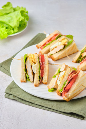 Club sandwiches with chicken, boiled egg, tomato and bacon on a white ceramic board on a light concrete background. american food. Sandwich Recipesの写真素材