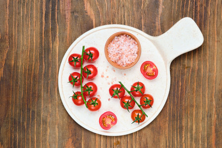 Cherry tomatoes with spices on a ceramic board on a brown wooden background. Culinary background, ingredients with place for textの写真素材