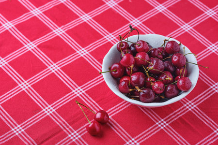 Ripe juicy cherries with water drops in a ceramic bowl on a table with a red tablecloth. Summer berries. Photo in one colorの写真素材