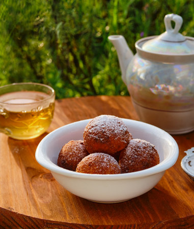 Round cottage cheese donuts, sprinkled with powdered sugar, in a white bowl on a round wooden background. donut recipes. outdoor tea drinkingの写真素材