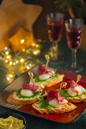 Mini sandwiches with pear, smoked duck and arugula in the shape of a Santa Claus hat on a square plate on a green concrete background. Merry christmas concept. christmas party snacksの写真素材