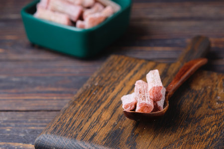 Candied rhubarb, sprinkled with powdered sugar, in a ceramic plate on a purple wooden background. Preparations, conservation. Rhubarb recipes. Candied fruits, dried fruits.の写真素材