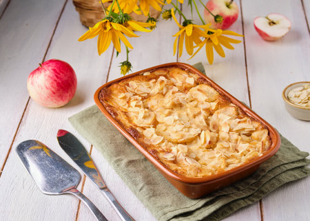 French apple pie, sprinkled with almond petals, in a rectangular brown ceramic form on a light wooden background. Recipes for apples, baking. French cuisineの写真素材