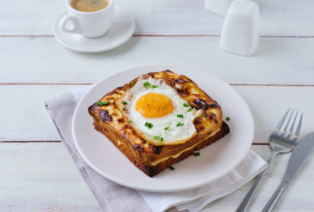 Hot croque madame sandwich with ham, cheese and fried egg on a white plate on a light wooden background. Sandwich recipes, hot breakfasts. French cuisineの写真素材