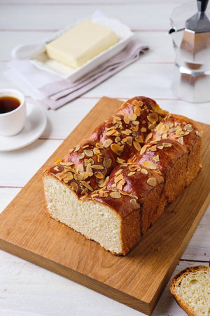 Butter brioche bread sprinkled with almond petals on a wooden board on a light concrete background....