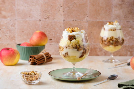 Dessert, portioned apple trifle with oat crumble, spiced cake, custard and whipped cream in a glass goblet on a light concrete background. Apple desserts, portioned desserts in glassesの写真素材