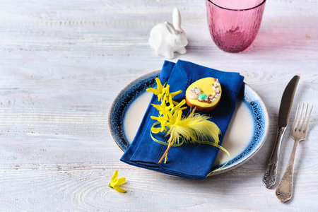 Easter table setting with blue napkins, burgundy water glasses and yellow decor on a wooden table....