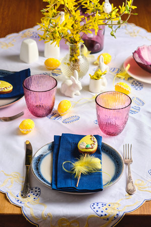 Easter table setting with blue napkins, burgundy water glasses and yellow decor on a wooden table...