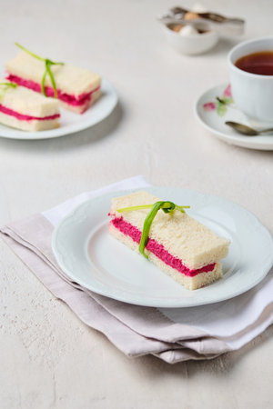 Tea sandwiches on white bread with beetroot hummus on a light ceramic plate on a light concrete background. Sandwiches for tea, light snacks.の写真素材