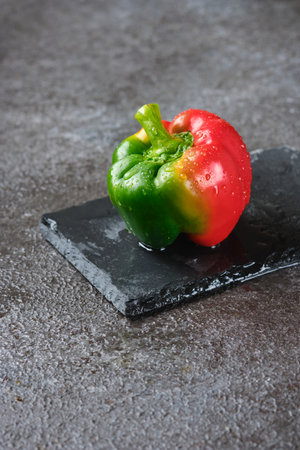 Fresh bicolor red and green bell pepper with water droplets on black concrete background. Fresh vegetables, veganの写真素材