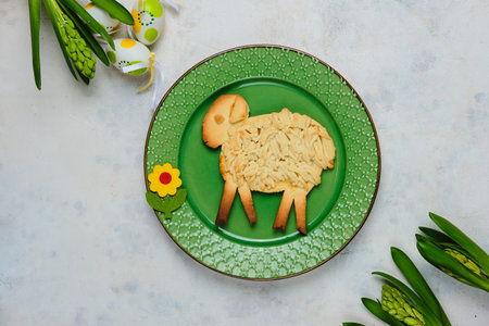 Easter pastries, shortcrust pastry lamb on a green plate on a light concrete background with Easter decor. Easter concept, sweetsの写真素材