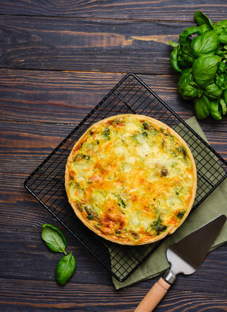 Unsweetened pastry, a whole quiche with spinach, oyster mushrooms, egg filling and cheese on a baking rack on a dark wooden background. Spinach recipes. Snack pies. French cuisine.の写真素材