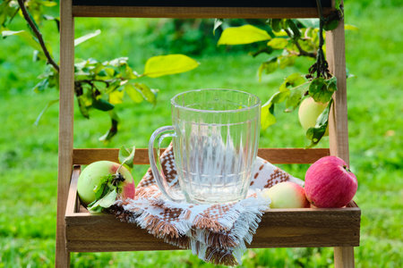 Empty glass mug for soft drinks on a wooden stand under fruit trees in the garden.の写真素材