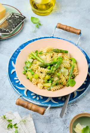 Pasta primavera, fusilli with green peas, asparagus and parmesan cheese in a ceramic plate on a gray concrete background. Asparagus recipes. Italian Cuisine. Seasonal products.の写真素材