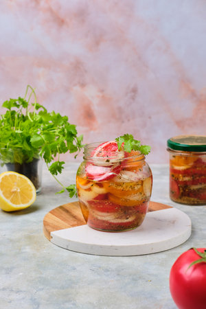 Salad sliced ââfast pickled tomatoes with onions in a glass jar on a gray concrete background. Harvesting, conservation, pickled vegetables. Tomatoes recipesの写真素材