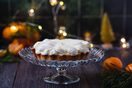 Christmas mini tart with mandarin filling and cream on glass cake stand on dark wooden background. Holiday desserts. Merry Christmasの写真素材